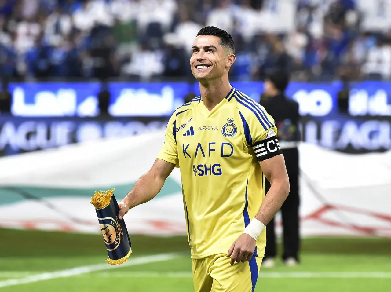 Uśmiechnięty Cristiano Ronaldo w żółtej koszulce Al Nassr trzyma zwiniętą flagę. Zastanawiasz się, ile zarabia Ronaldo na minutę?