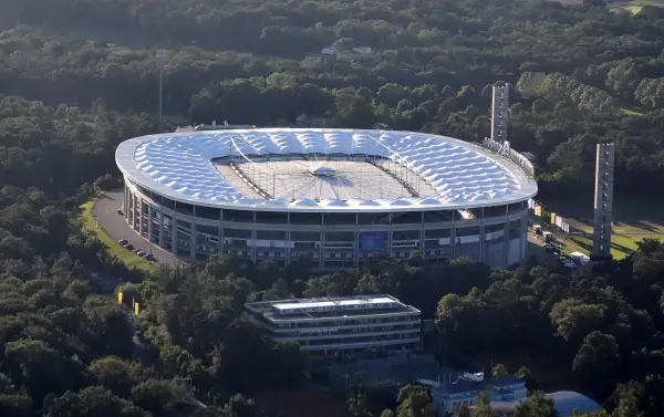 Stadion piłkarski otoczony drzewami, z charakterystycznym białym dachem.